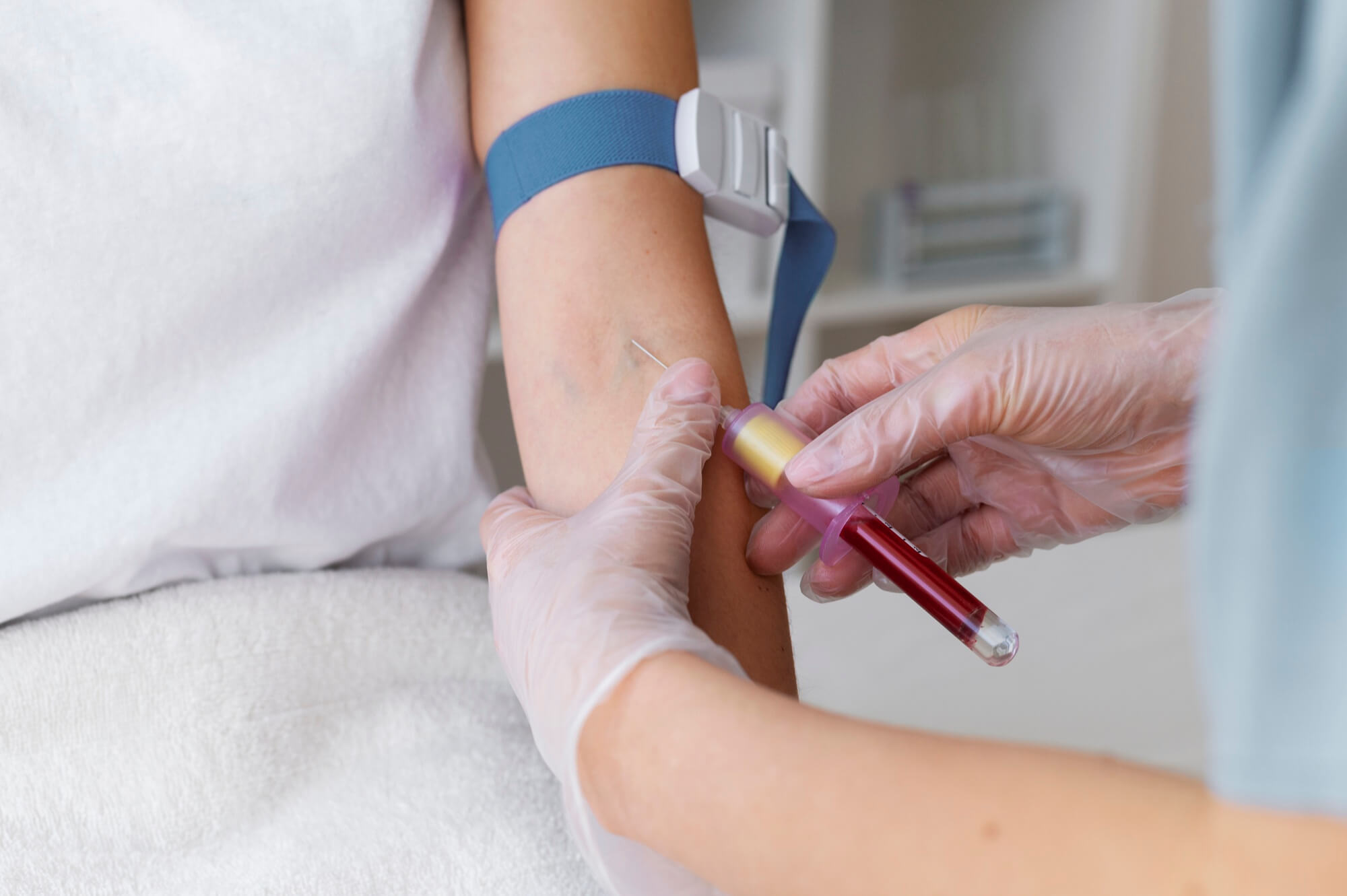 Health worker in gloves drawing blood from a patient's arm with a tourniquet in place